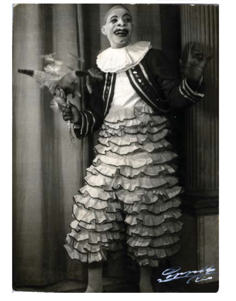 Uma fotografia preta e branca registra o artista Benjamim de Oliveira vestido e maquiado de palhaço.