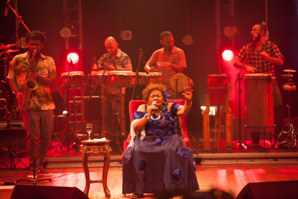 Imagem colorida que mostra Dona Onete e sua banda se apresentando durante o show do DVD Flor de Lua.